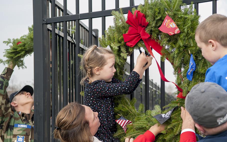 Lola Worcester, held up by her mom Renee, cinches a tie band as she helps hang a large ceremonial wreath at the Pentagon in Arlington, Va., on Friday, Dec. 11, 2015. Lola's brother, Miles, looks on as his father, Mike, holds him up. At Friday's event, dozens of volunteers helped hang 184 wreaths to honor the victims who died on Sept. 11, 2001, when a hijacked aircraft was crashed into the side of the Pentagon. Mike Worcester's father, Morrill, is owner of the Worcester Wreath Company in Harrington, Maine. The Worcerter clan formed the non-profit Wreaths Across America in 2007 and has provided hundreds of thousands of wreaths each holiday season to be laid a grave sites across the nation.