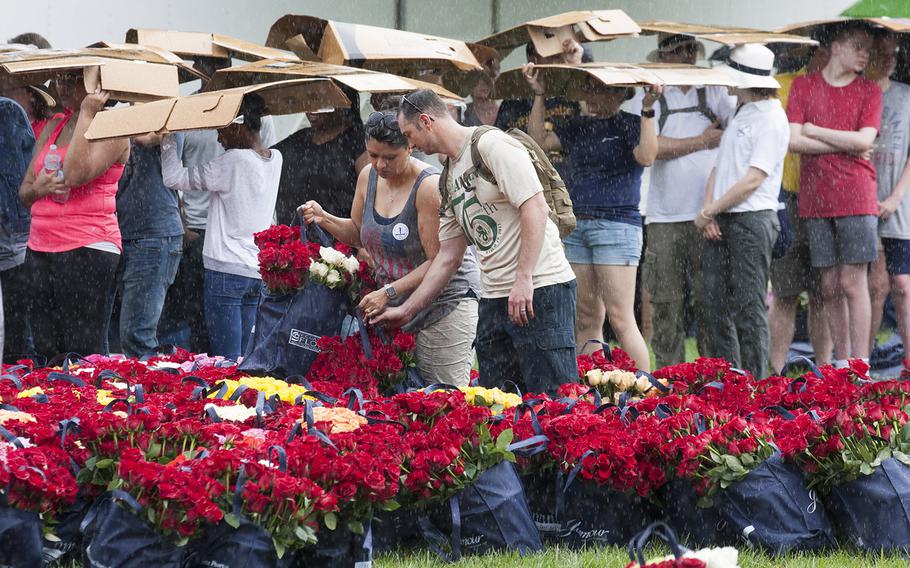 Volunteers pick up bags of roses to be placed at Arlington National Cemetery graves as others waiting to register seek shelter from a sudden downpour during an event organized by the Memorial Day Flowers Foundation on Sunday, May 28, 2017.