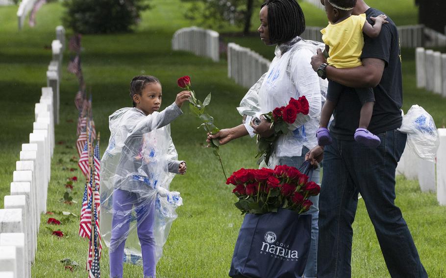 U.S. Marine Corps Staff Sgt. Angelica Danner hands a rose to six-year-old Liana Danner to place at an Arlington National Cemetery grave as Marine Staff Sgt. Marvin McCammon, holding Mikayla McCammon, watches during an event organized by the Memorial Day Flowers Foundation on Sunday, May 28, 2017.