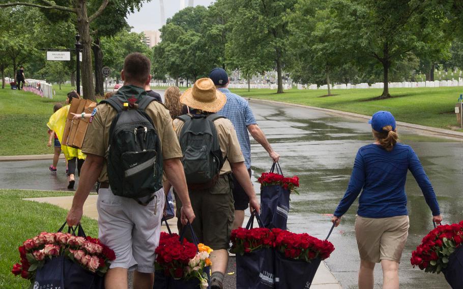 With the U.S. Air Force Memorial in the background, volunteers carry bags of roses to be placed at Arlington National Cemetery graves during an event organized by the Memorial Day Flowers Foundation on Sunday, May 28, 2017.