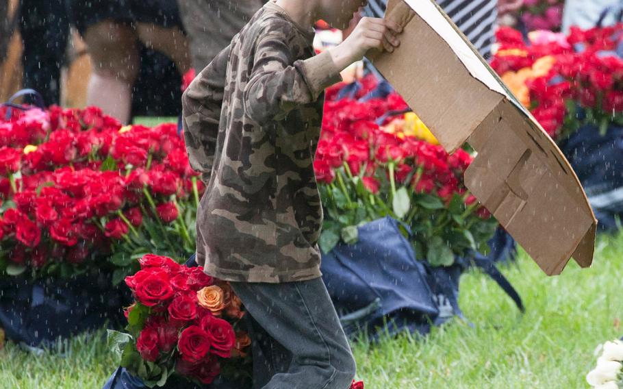 A young volunteer shields himself against a sudden downpour as he carries roses to be placed at Arlington National Cemetery graves during an event organized by the Memorial Day Flowers Foundation on Sunday, May 28, 2017.