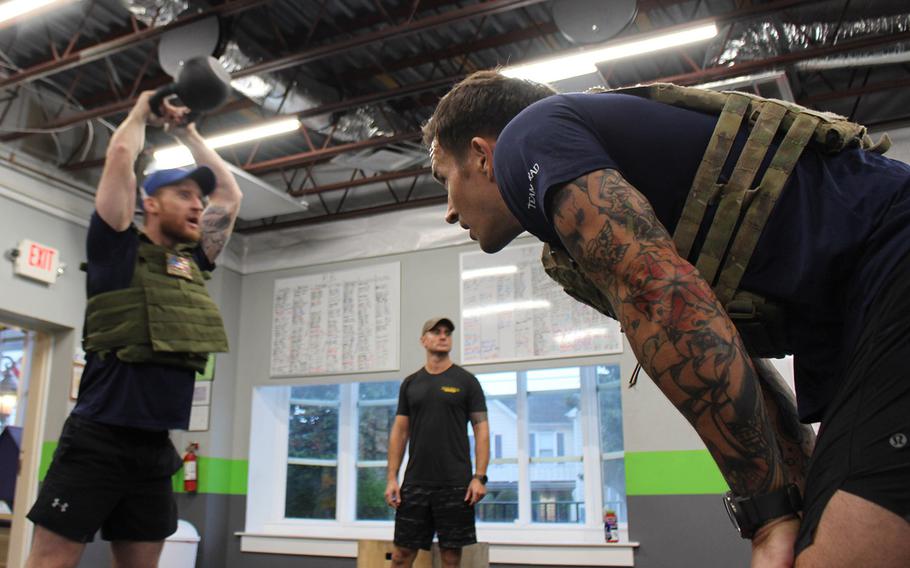 U.S. Navy Lt. Nick Matics watches former EOD technician and Paralympian Brad Snyder lift a kettle bell in front of Siggy Herrmann, co-owner of Coal Road Crossfit in La Planta, MD. The men all participated in a commemorative workout to support the EOD Warrior Foundation.