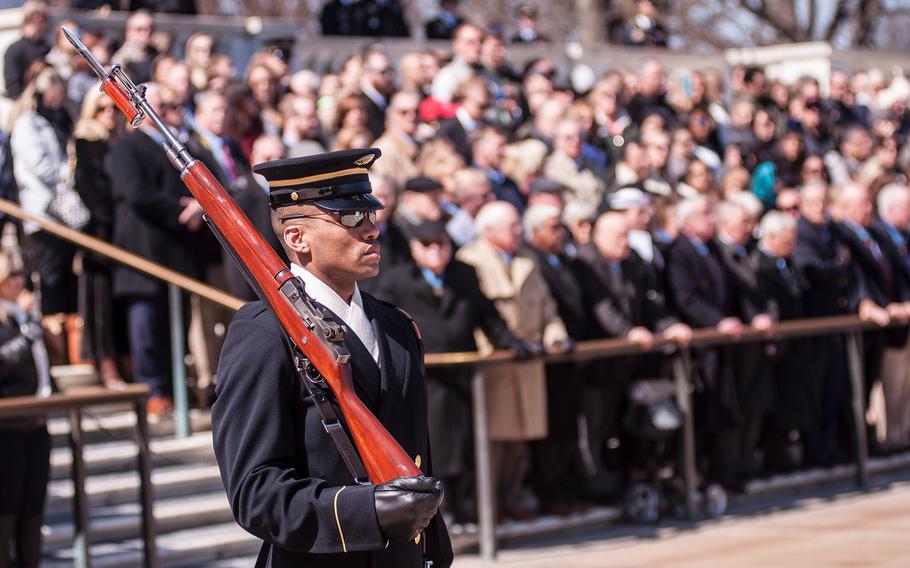 A crowd of onlookers, including more than two dozen Medal of Honor recipients, watch an Army sentry perform his guard duties before the start of a special wreath-laying ceremony at Arlington National Cemetery's Tomb of the Unknowns on Friday, March 23, 2018.
