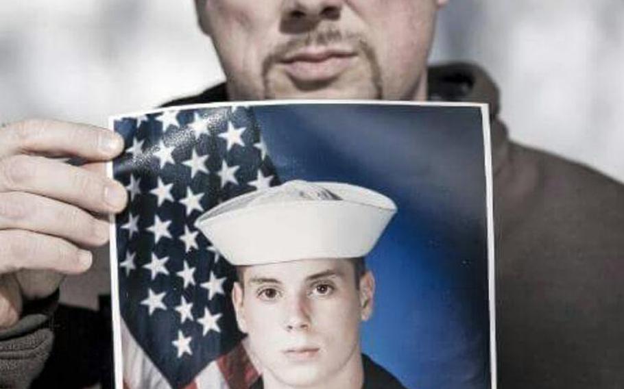 Heath Phillips displays a photo of himself at age 17, shortly after joining the Navy.