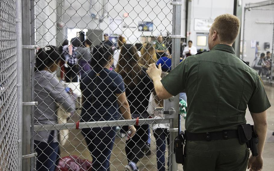 In this photo provided by U.S. Customs and Border Protection, a U.S. Border Patrol agent watches as people who've been taken into custody related to cases of illegal entry into the United States, stand in line at a facility in McAllen, Texas, Sunday, June 17, 2018.