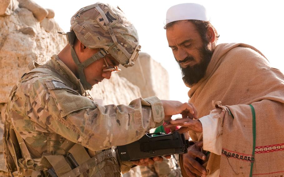 U.S. Army Pfc. Mark Domingo, left, takes an Afghan man's fingerprints in the village of Dande Fariqan, in Afghanistan's Khowst province on Nov. 5, 2012. Domingo, who converted to Islam and discussed launching various terror attacks throughout Southern California, was arrested as he plotted to bomb a white supremacist rally, federal prosecutors said Monday, April 29, 2019.