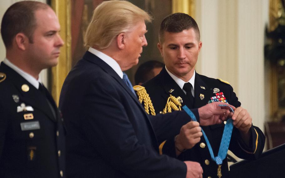 A White House military aide hands off a Medal of Honor award device to President Donald Trump during a ceremony at the White House on Wednesday, Oct. 30, 2019. The award was presented to Army Master Sgt. Matthew Williams, at left, for bravery under fire against enemy forces in an April 2008 battle in Afghanistan.