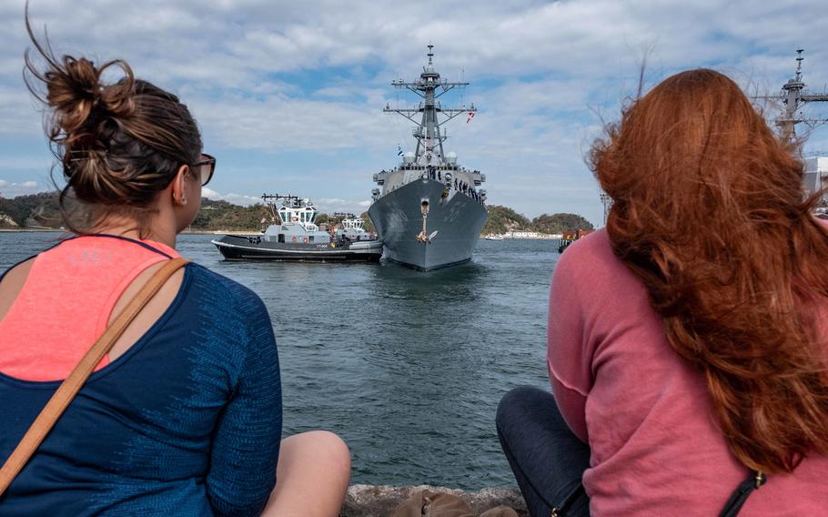 Onlookers sit on a pier as the USS John S. McCain departs Yokosuka, Japan, Oct. 28, 2019, to conduct comprehensive at-sea testing, the ship's first underway since its collision in 2017.