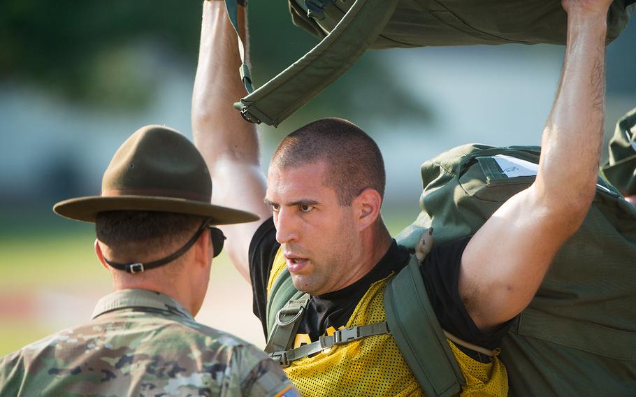 In a July, 2018 photo, Spc. John Strezo from Burlington, Mass., holds his duffel above his head as initial entry trainees arrive at Echo Company, 2nd Battalion, 19th Infantry Regiment, on Fort Benning, Ga., for the first day of the 22-week pilot program for One Station Unit Training for Infantry soldiers.