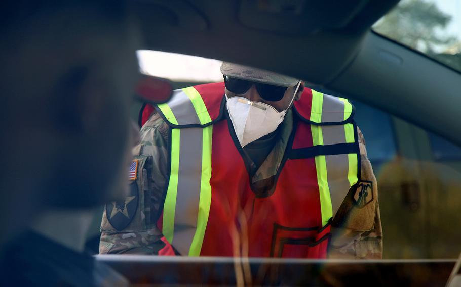 U.S. Army Reserve Sgt. Andre Lewis with the 7th Mission Support Command asks COVID-19-related screening questions to occupants of a car before they can enter  Daenner Kaserne in Kaiserslautern, Germany, March 19, 2020. 