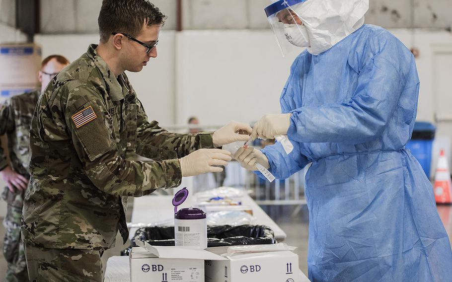 U.S. Army Spc. Gabriel Eiter, left, a small arms/artillery repairer assigned to the 3637th Maintenance Company, Illinois Army National Guard, and Lt. Col. Jim Avery, a flight surgeon assigned to the 126th Medical Group, Illinois Air National Guard, handles COVID-19 testing equipment at a drive-thru testing site in Bloomington, Ill., March 28, 2020.