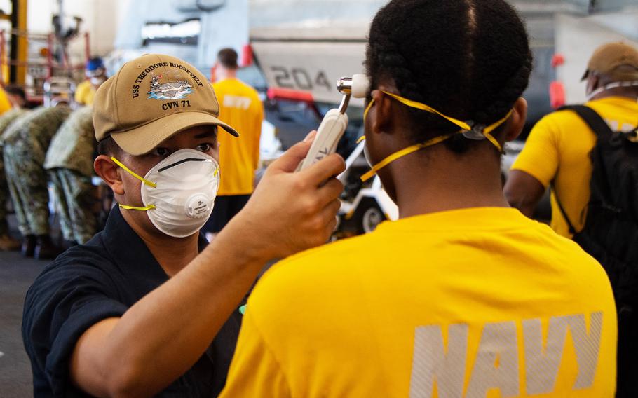 Sailor David Romero takes the temperature of another sailor assigned to the aircraft carrier USS Theodore Roosevelt on April 10, 2020.