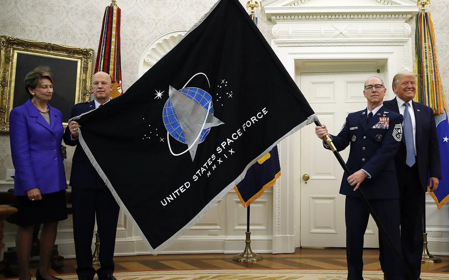 President Donald Trump stands as Chief of Space Operations at US Space Force Gen. John Raymond, second from left, and Chief Master Sgt. Roger Towberman, second from right, hold the United States Space Force flag as it is presented in the Oval Office of the White House, May 15, 2020, in Washington. Secretary of the Air Force Barbara Barrett stands at far left.