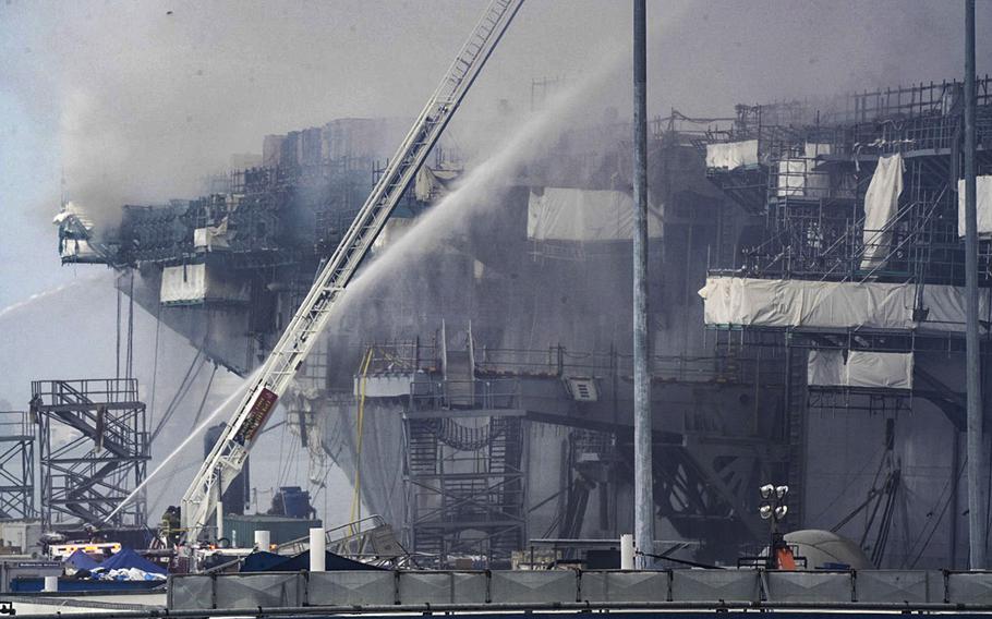 In a Monday morning, July 13, 2020 photo, under a cloud of smoke the fire continues to burn aboard Bonhomme Richard at San Diego Naval Base.