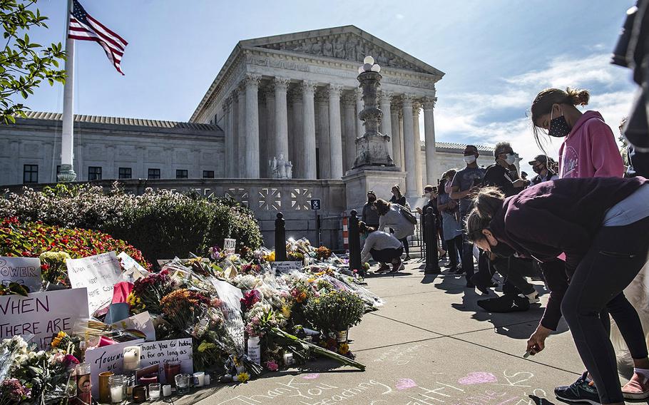 Mourners leave flowers and messages on the sidewalk outside the Supreme Court in Washington, D.C., on Saturday, Sept. 19, 2020, as the American flag is flown at half-staff in honor of the passing of Supreme Court Justice Ruth Bader Ginsburg.