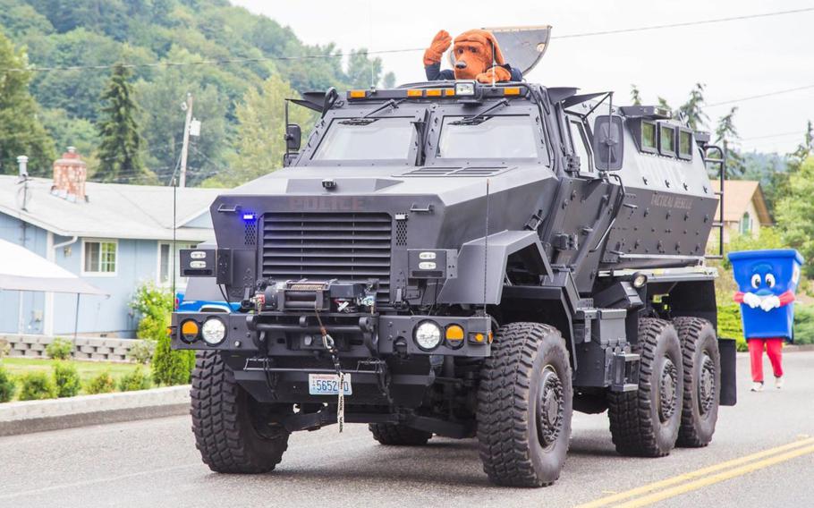 A surplus military mine-resistant armored personnel carrier drives down a street during a 2016 parade in Algona, Washington. The Snoqualmie Police Department acquired the vehicle as part of an equipment sharing program from the federal government. It is utilized by a coalition of small-city police departments.