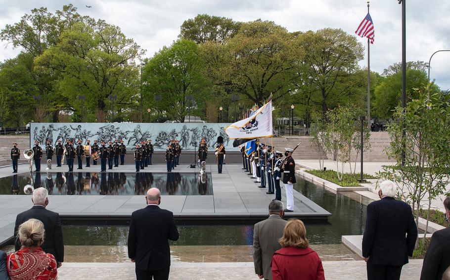 Dignitaries who were involved in promoting the new World War I Memorial stand at attention in the foreground as a military honor guard and the U.S. Army Band "Pershing's Own" take part in a dedication ceremony for the memorial in Washington, D.C., on Friday, April 16, 2021. In the background, the U.S. flag flies after it was raised for the first time at the site.