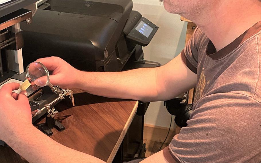 Former Army Capt. Andy Reed looks through a magnifying glass as he engraves a plaque to go on a presentation box for a first salute coin, April 28, 2021.
