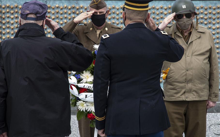 World War II veteran Harry Miller and Chaplain (Col.) Michael Shellman, foreground, and Vietnam-era veteran Sidney B. Wade Jr. and National Park Service volunteer and reenactor Patrick McCourt salute as they lay a wreath during a ceremony at the National World War II Memorial in Washington, D.C. on May 8, 2021, the anniversary of the end of the war in Europe.