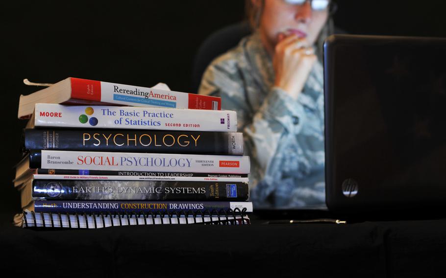 An airman looks at a computer screen next to school textbooks on a table.
