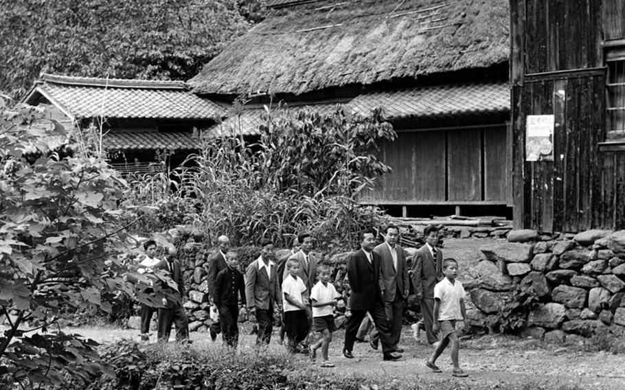 Rep. Daniel K. Inouye (D-Hawaii), in dark suit, strolls through the mountain village of Yokoyama, Japan, his ancestral home, in 1960.