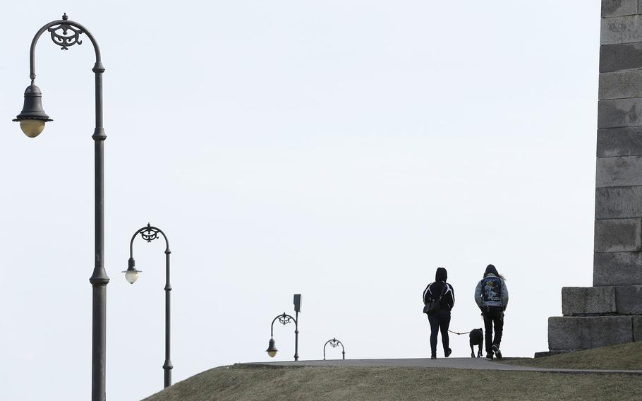 Stephanie Rosario, left, and Mat Spitkovsky, right, both of Boston, walk Rogue, a 2-year-old Pit Bull mix, along a path around Fort Independence, right, on Castle Island, in Boston's South Boston neighborhood on April 6, 2015.