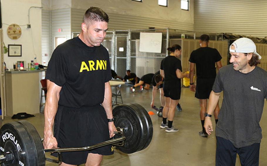 Maj. Timothy Cox lifts weights during physical training while the lead strength coach of 22nd Chemical Battalion, Mike Edwards, supervises him in the fitness training facility at Fort Bliss, Texas. Cox set a new standard by obtaining a 600, the highest score ever recorded, on the Army Combat Fitness Test.