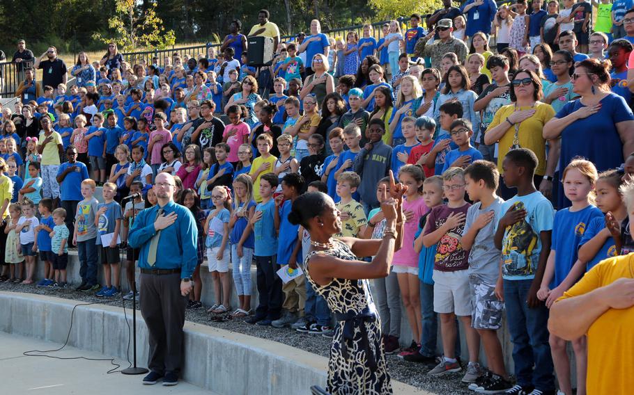 Administrators, teachers and students observe the national anthem in September 2018, while celebrating the opening of E.A. White Elementary School at Sand Hill at Fort Benning, Ga. Schools at Fort Benning are among Pentagon-run schools in the U.S. where teachers work an extra 30 minutes each workday without pay.
