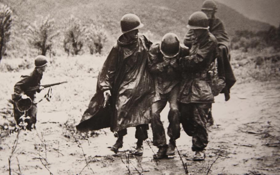 An iconic photograph of Father Emil Kapaun, right, shows him and Capt. Jerome A. Dolan, left, a medical officer, carrying an exhausted GI off a battlefield in Korea, early in the war.