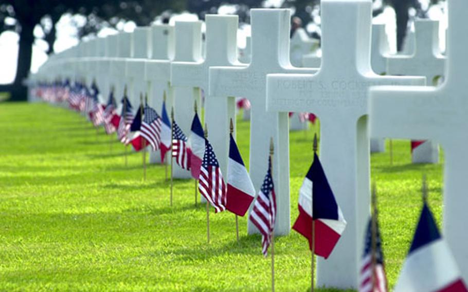 Rows of crosses and Stars of David stand in long rows at Normandy American Cemetery, Colleville-sur-Mer, France, decorated with American and French flags. The cemetery is the final resting place for 9,386 of our war dead. 