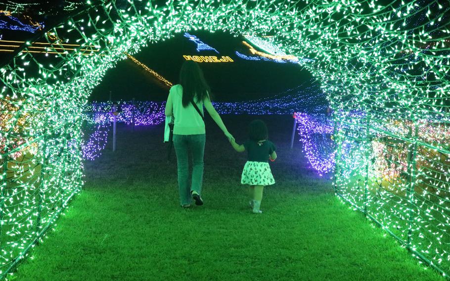 Mother and daughter holding hands as they walk under a tunnel at Noheji Illumination HIkari Story