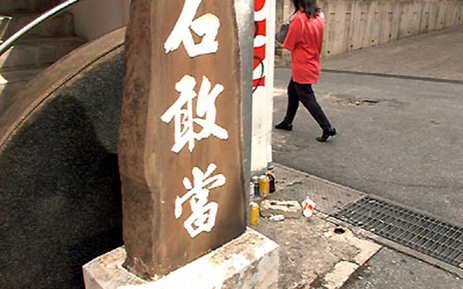 An Ishi-Gan-To stone marker stands on a corner of a condominium in Naha. Okinawans believe that evil spirits dwell in dead ends and street corners. The three Chinese characters are "magic" words to deflect the devil.