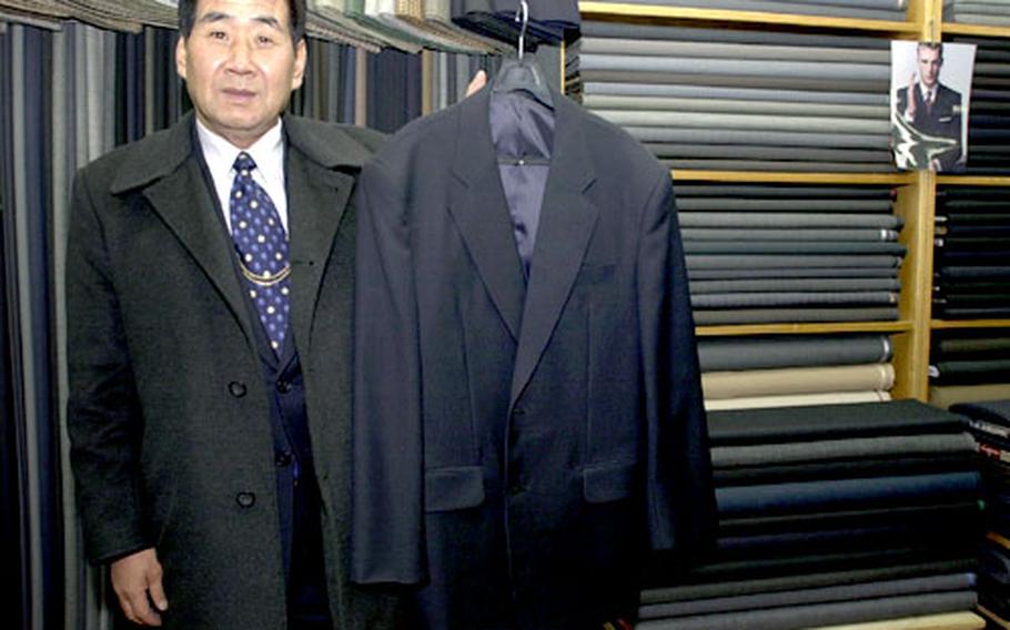 Mr. Mike Min, also known as “Buddy Hackett,” holds up one of his custom tailored suits inside his shop in the Itaewon section of Seoul, South Korea. Tailormade suits can be purchased at his shop, and countless others, for about a quarter to a third the price of a suit tailormade in the United States.