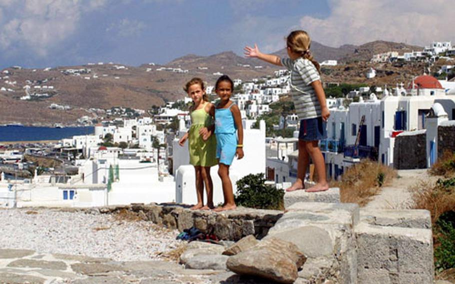 Barefoot and having fun in the nice weather, little girls stand on a few cobblestones that surround the Boni Windmill, one of the best preserved on the Greek island of Mykonos.
