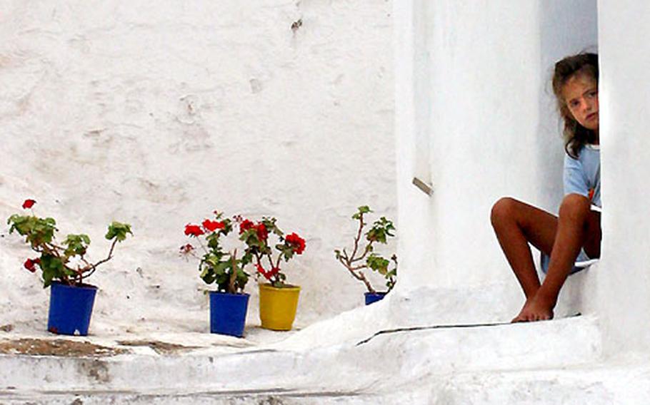 A girl sits on a Mykonos porch watching the photographer take a photo.