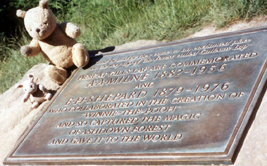 Two stuffed bears — one based on the Disney movies, one on the original drawings by Ernest Shepherd — sit next to a plaque honoring A.A. Milne, author of the "Winnie the Pooh" stories, and Shepherd, who illustrated the book. The plaque is in the Ashdown Forest, real-life site of the "Pooh" stories.