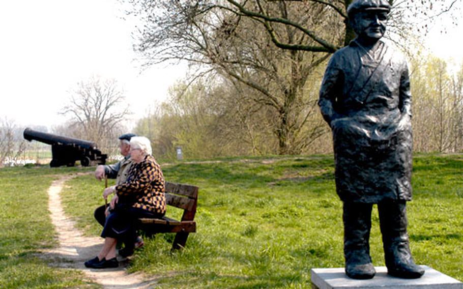 An elderly couple sit on a bench atop Woudrichem’s ramparts watching the ships ply the Waal river. In the foreground is a statue known as the Zalmvisser, or salmon fisher. Fishing was once a mainstay of the locals, but unfortunately there are no salmon left in Dutch rivers. In the background at far left is Loevestein Castle, across the Maas river from Woudrichem.