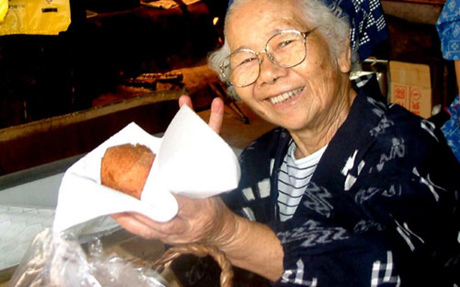 Tsuru Higa, 86, offers a visitor the tradional Okinawa doughnut at Ryukyu Mura, a folk village in Onna.