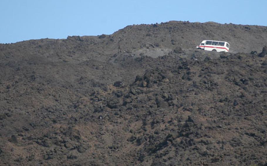 A four-wheel-drive bus crawls through a lava trail up the side of Mount Etna.