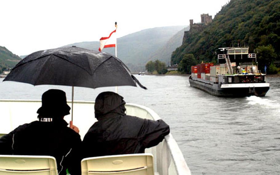 Passengers brave a sudden rain shower on the Rhine as their ship passes a container ship and Burg Reichenstein. While most ships have covered areas below deck, some riders prefer to stay outside for a better view.