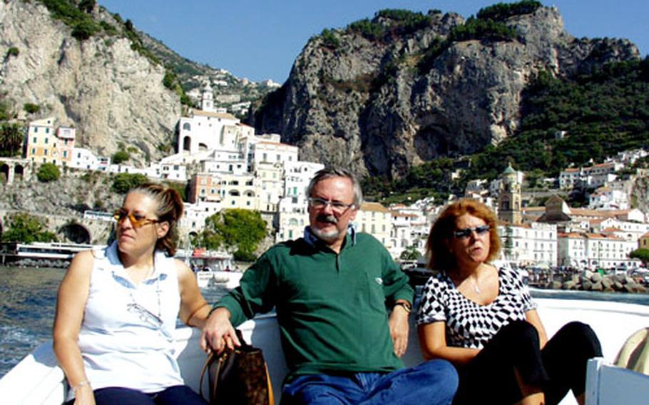 Tourists relax on a boat trip from the town of Amalfi, shown in the background. Several boat tours operate around the Amalfi Coast, taking visitors to secluded inlets.