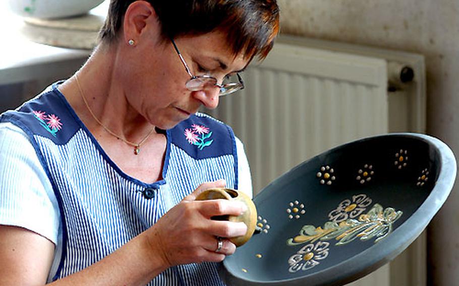 A woman decorates a shallow bowl with traditional Alsatian designs.