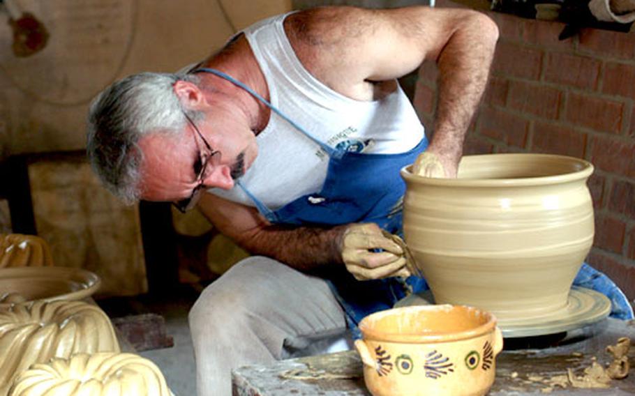 A potter bends to shape a bowl in his workshop.