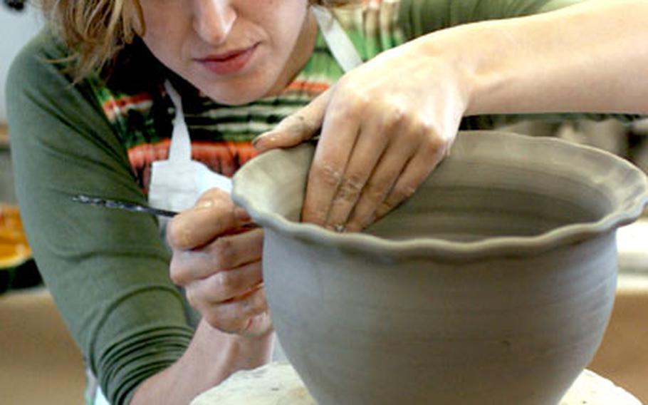 Working her craft at a pottery shop in Soufflenheim, this potter&#39;s assistant is cutting decorative holes in a vase.