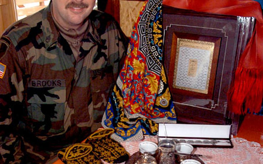 Staff Sgt. Richard Brooks of Task Force Renegade displays the gifts he bought in Bosnia for his family — a doily made by a woman from a refugee camp his task force sponsors, a traditional Bosnian copper coffee set with mini cups, silk scarves, woolen slipper-socks and a framed work of art with 99 names for Allah written in gold in Arabic.