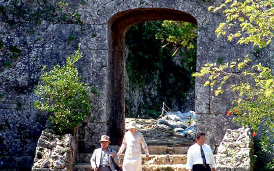 Tourists walk down the steep stone steps of the great archway of the castle ruins.