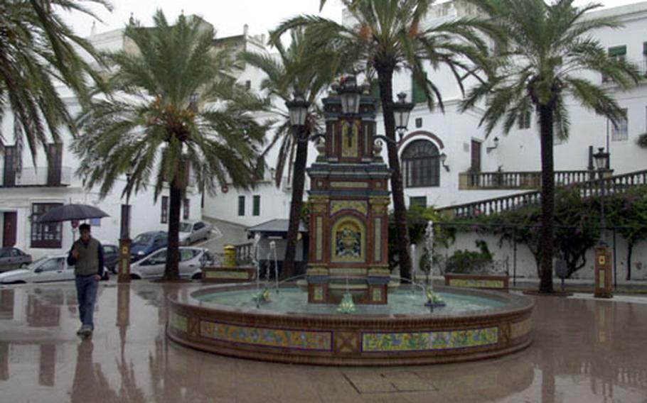 A man walks by an ornate ceramic fountain in the center of Plaza de España, a popular meeting place in Vejer de la Frontera with cafes, bars and restaurants ringing the perimeter.