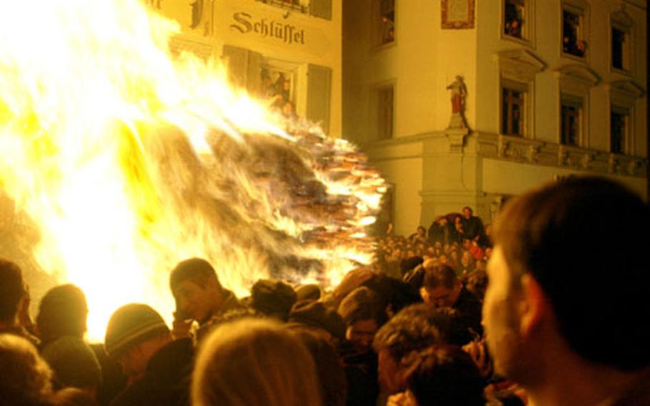 One of the wagons filled with burning wood creates enormous flames and heat. The first rows of spectators turn their heads and move backward to protect themselves.