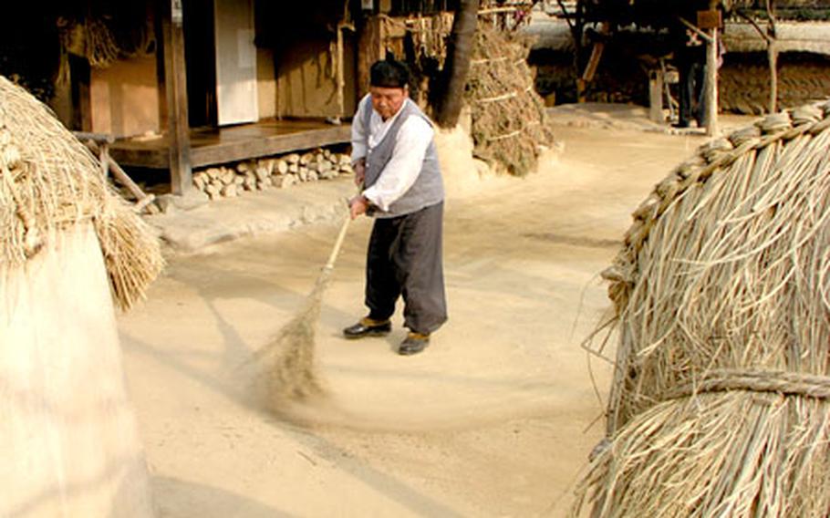 A man dressed in traditional Korean garb sweeps the ground in Minsokchon.