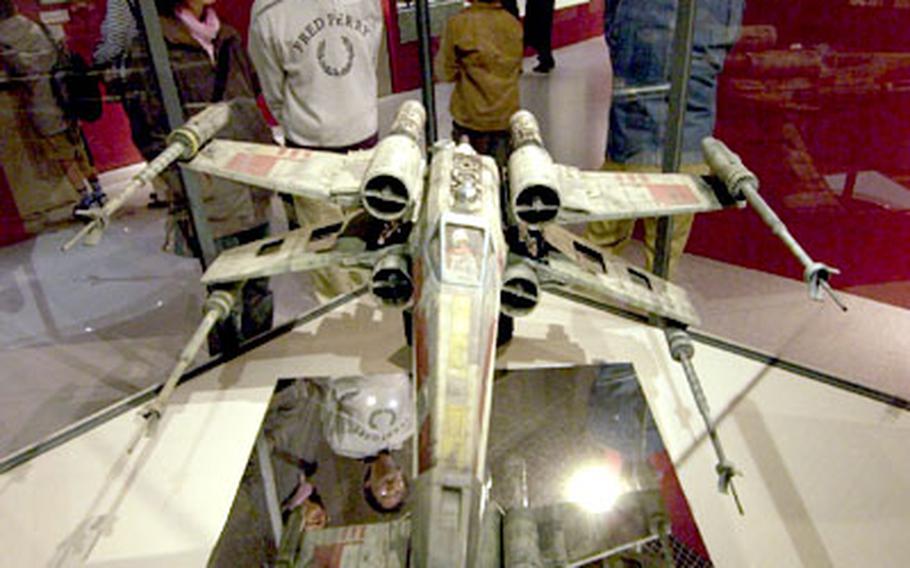 A couple looks at a Rebel X-Wing Fighter on display.